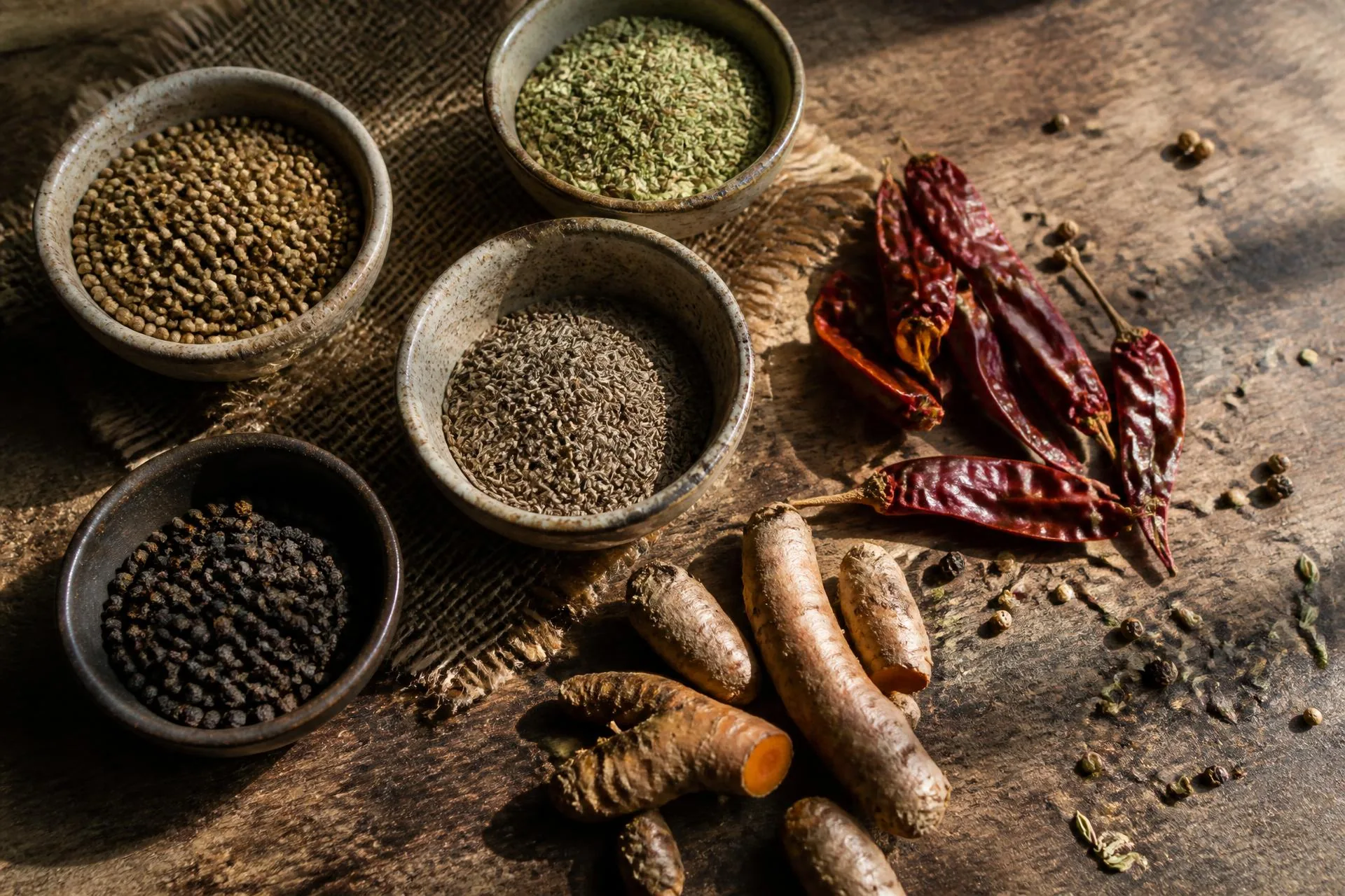 Indian cumin, coriander, black pepper, dried chillies and turmeric arranged in ceramic bowls on a weathered wooden table